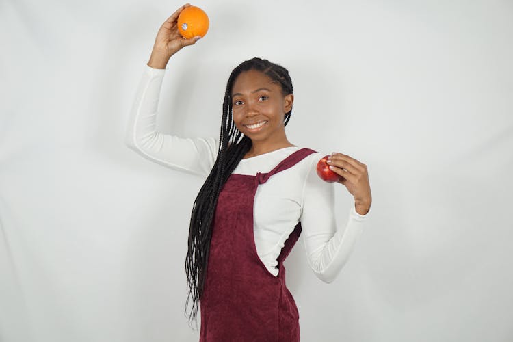 A Woman Holding An Apple And Orange Fruits