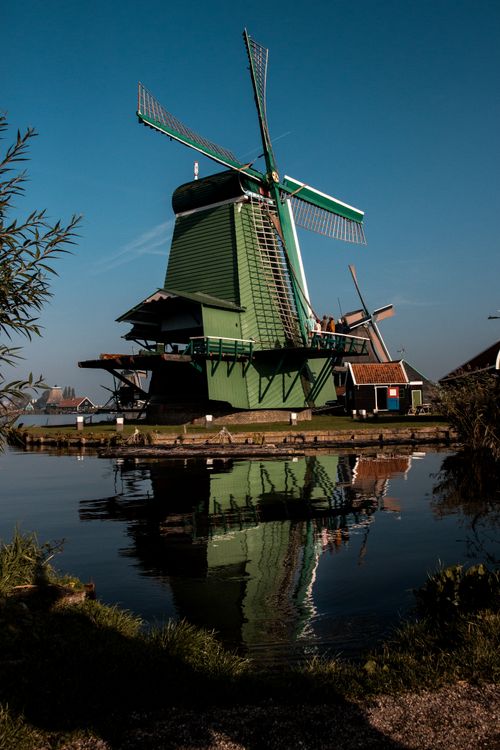 Free Scenic view of traditional Dutch windmill reflecting in water under a clear blue sky in Amsterdam. Stock Photo