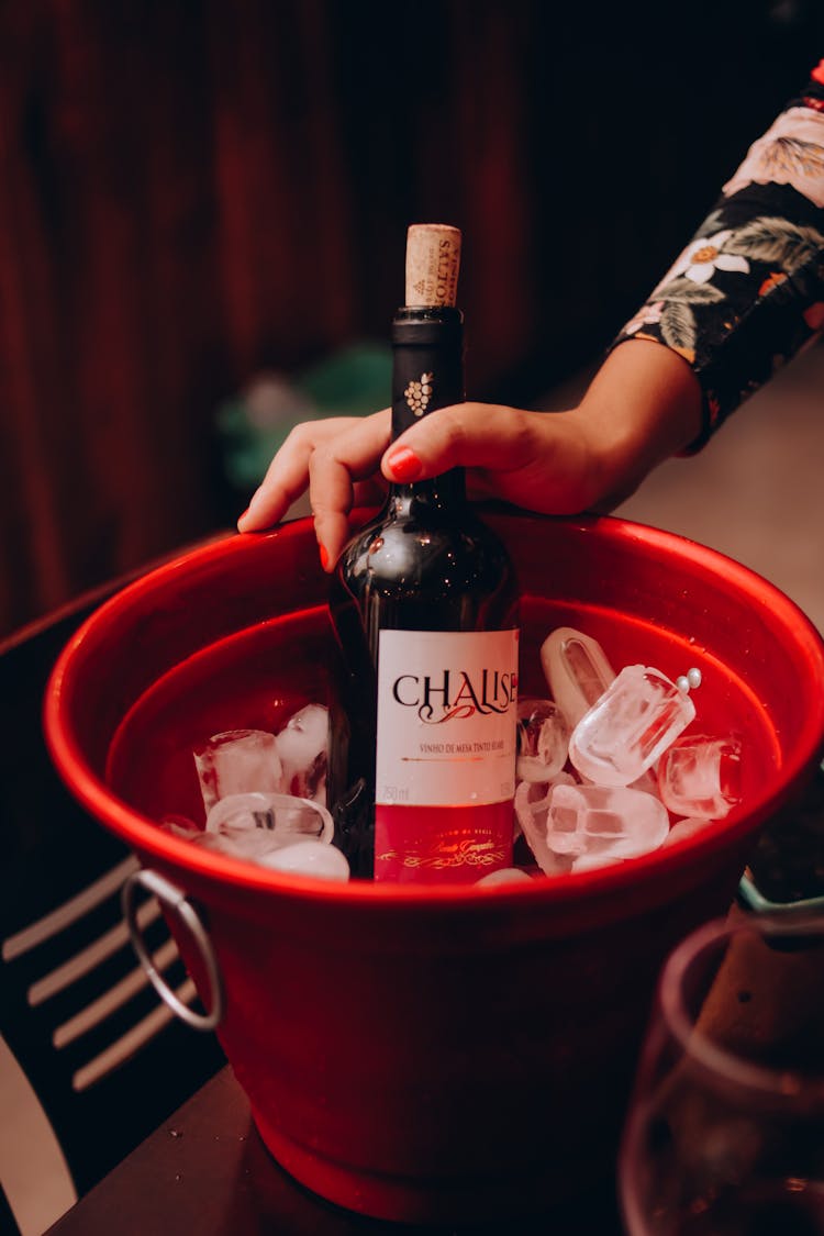 Person Holding Wine Bottle In Red Bucket