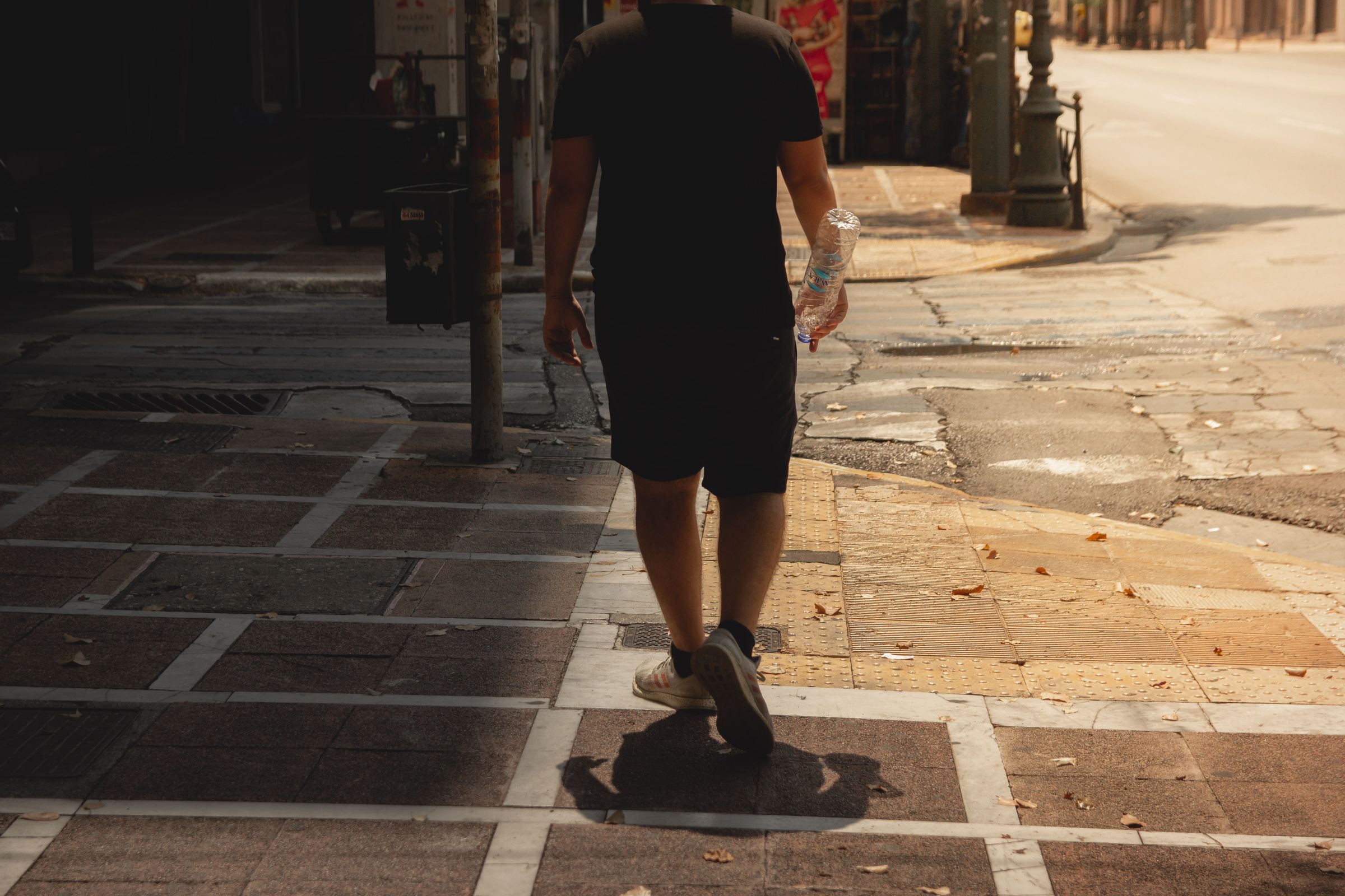 Person walking on a sunlit sidewalk in light clothing during extreme summer heat