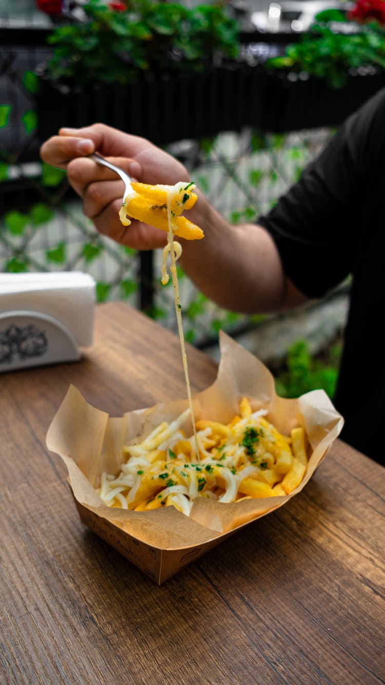A Person Eating A Cheesy French Fries