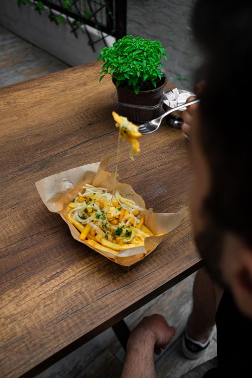 Free Vertical shot of cheese-topped French fries with a fork, taken indoors. Stock Photo