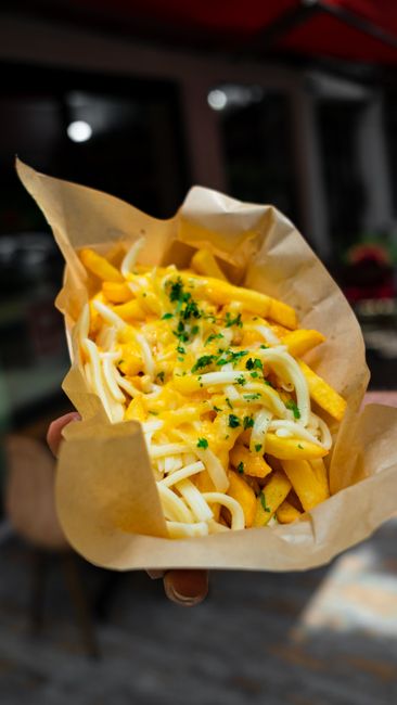 Golden cheese fries in paper cone with melted cheese sauce`