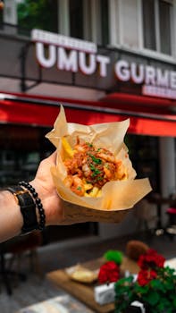 A hand holds tasty topped fries in front of a gourmet restaurant.