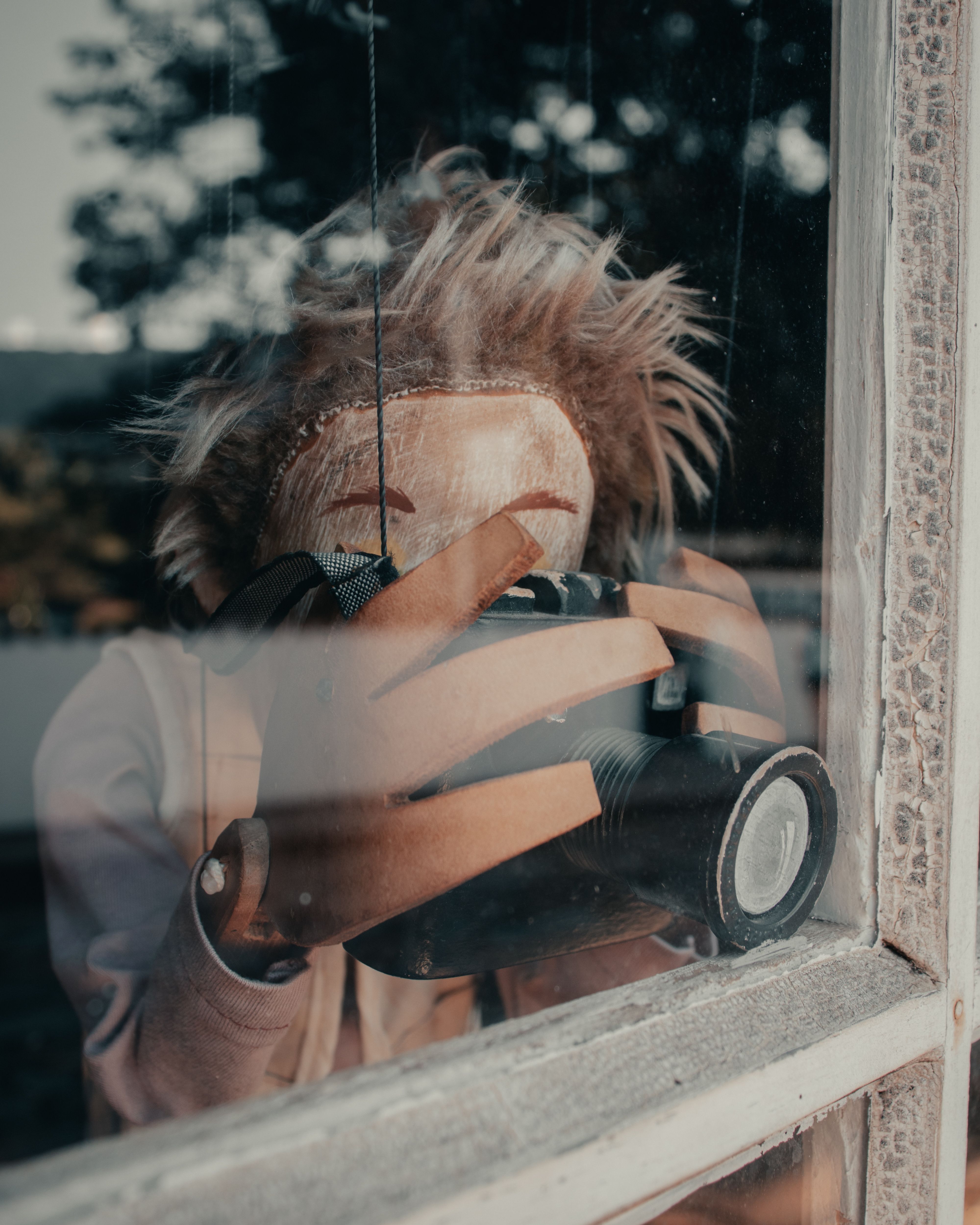 A puppet figure holds a camera behind a glass window in an artistic depiction.