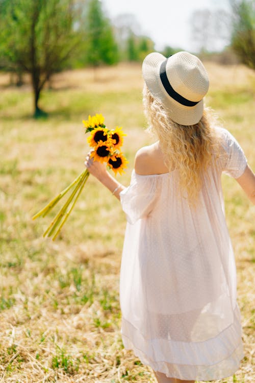 Free A Woman in White Dress Holding Yellow Sunflowers Stock Photo