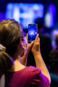 Woman records live concert on smartphone, showcasing technology in events.