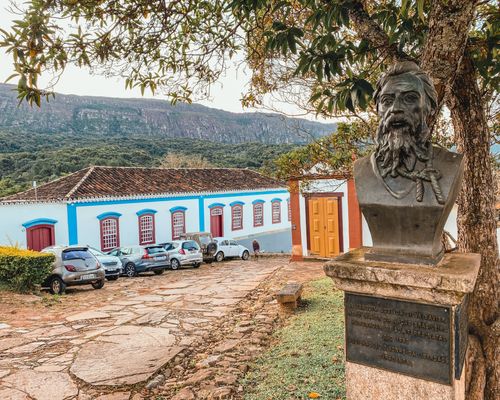 Free A scenic view of Tiradentes, Brazil featuring a historic bust, colonial buildings, and parked cars. Stock Photo