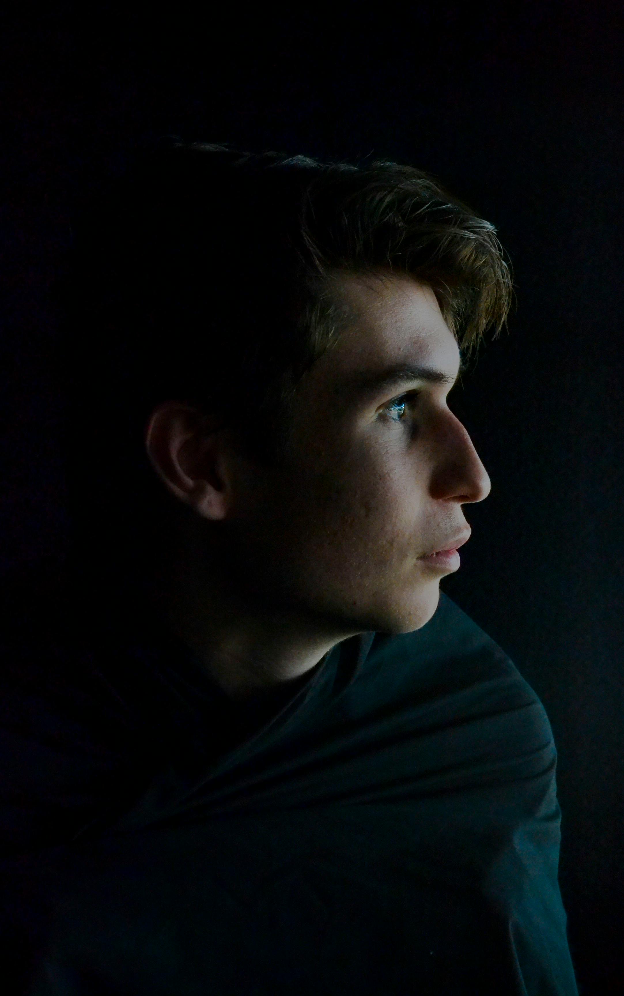 A contemplative young man gazes into darkness, side profile view, artistic moody tones.