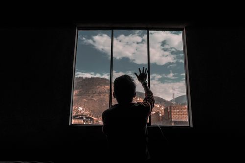 Free Silhouette of a person inside a room reaching towards a cloudy mountain view through a window. Stock Photo