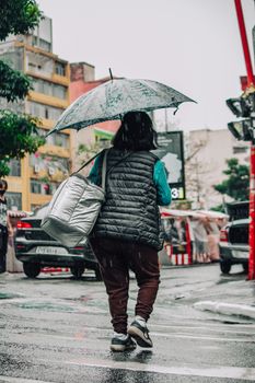A woman holding an umbrella walks across a zebra crossing in a rainy urban setting.