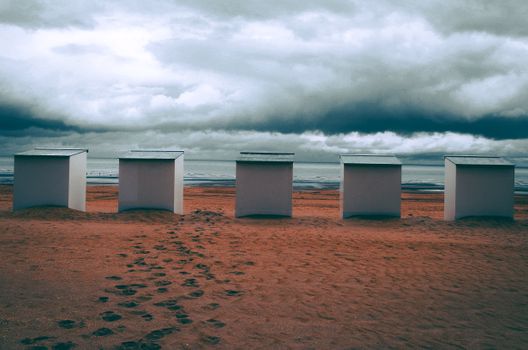Five beach cabins under cloudy skies on De Panne beach, Belgium.