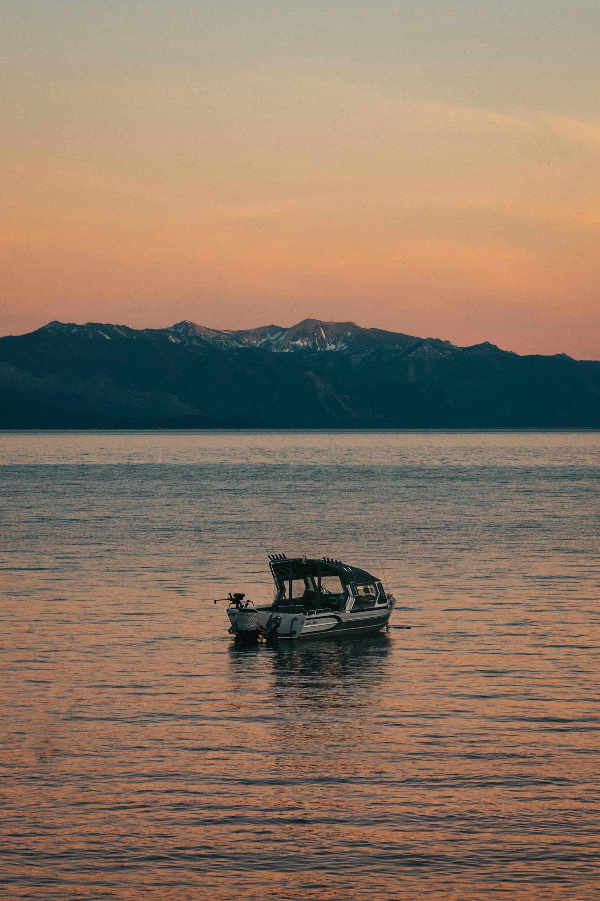 A tranquil scene of a boat on a calm lake at sunset with mountains in the background.