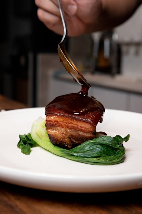 A Person Pouring Brown Sauce on Cooked Food on White Ceramic Plate