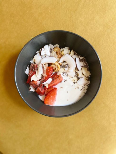 Healthy breakfast bowl with yogurt, strawberries, coconut, and seeds on a bright surface.
