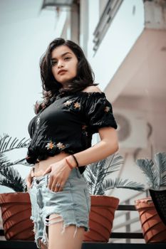 Stylish woman in black off-shoulder top and denim shorts standing outdoors.