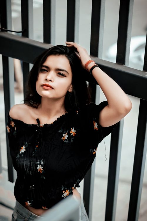 Free Young woman in a floral top poses against a city fence, exuding confidence. Stock Photo