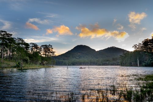 Free Tranquil lake view with a canoe, mountains, and trees at sunset, capturing peaceful nature. Stock Photo