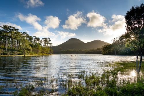 Free Beautiful landscape of a tranquil lake with surrounding pine forests and distant mountains at sunrise. Stock Photo