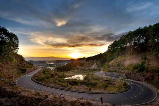 A beautiful sunrise over a winding mountain road surrounded by lush trees and nature.