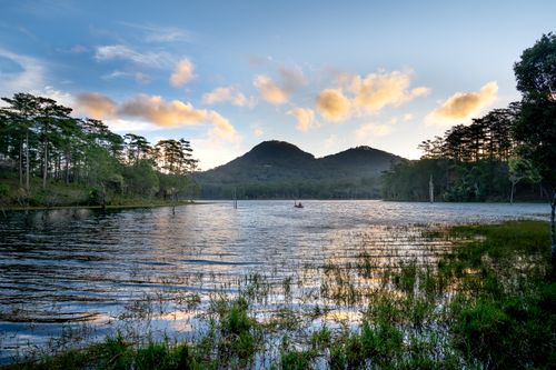 Free Peaceful mountain lake reflecting the sunrise sky, surrounded by trees and natural beauty. Stock Photo