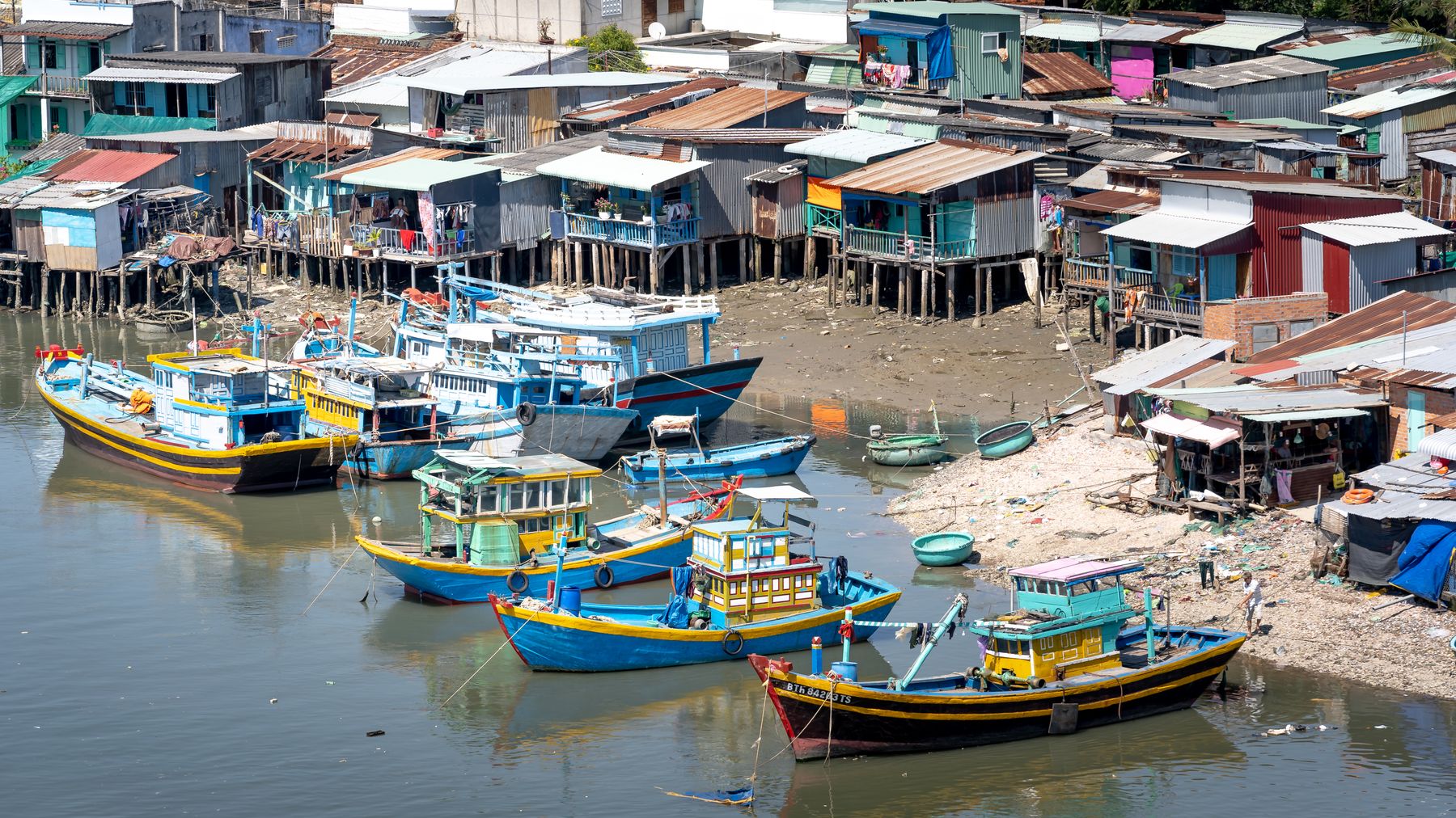 Colorful fishing boats docked by stilt houses in a traditional Vietnamese village.