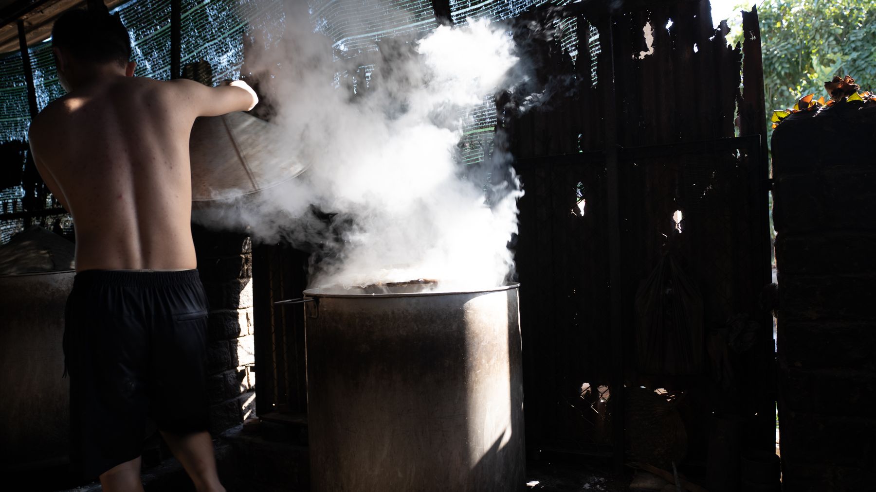 A man cooking traditional Vietnamese food in an open market with steam rising from the pot.