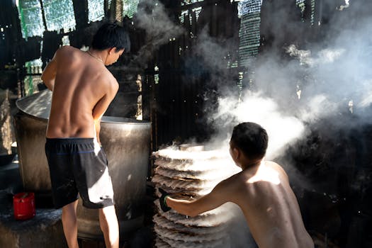 Two men cooking noodles in a smoke-filled traditional kitchen indoors, showcasing authentic culinary techniques.