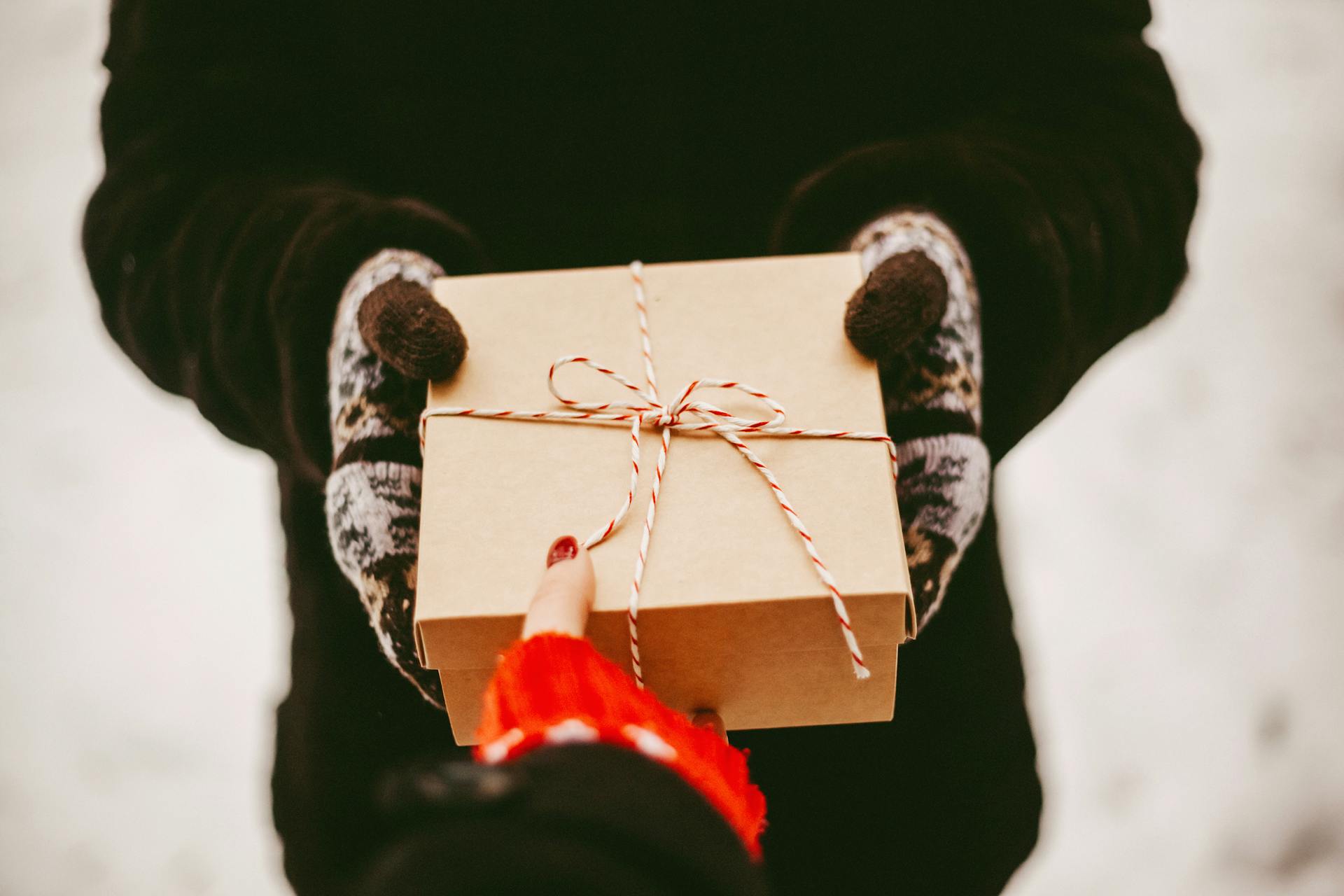 Warm winter scene of gloved hands exchanging a neatly wrapped gift outdoors.