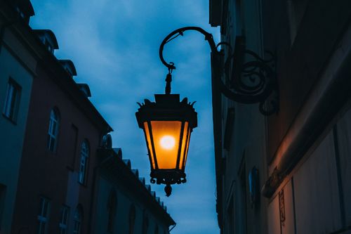 Free An illuminated streetlamp hangs elegantly between historic buildings as dusk sets in. Stock Photo