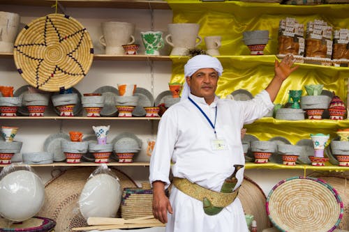 Free Man in Traditional Clothing Showing Products on the Shelf  Stock Photo