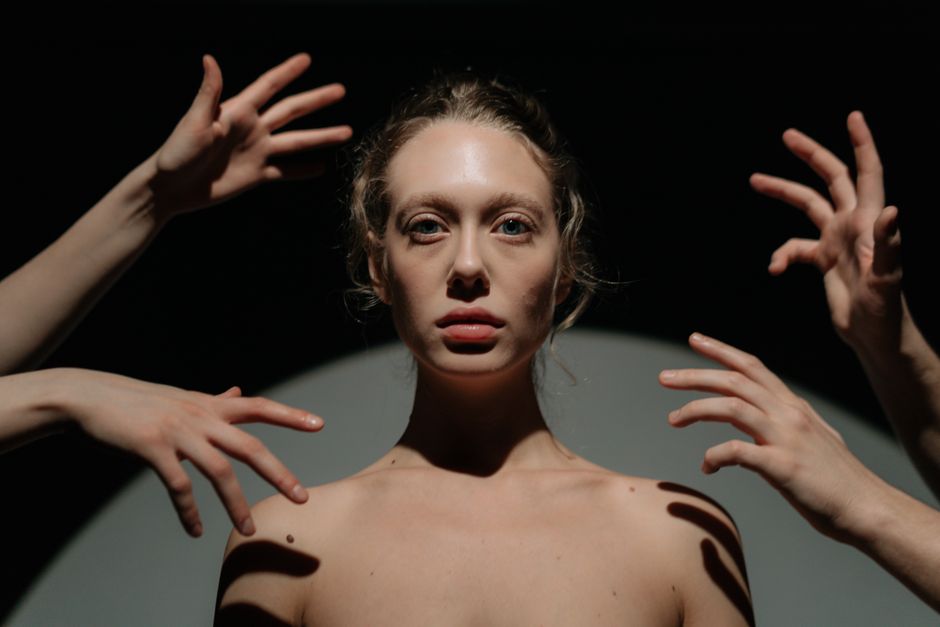 Artistic portrait of a woman surrounded by hands and shadows, creating a dramatic effect.