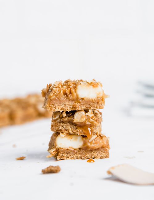 Stacked no-bake plant-based protein bars on parchment paper, showing a dense oat and peanut butter texture studded with chocolate chips.