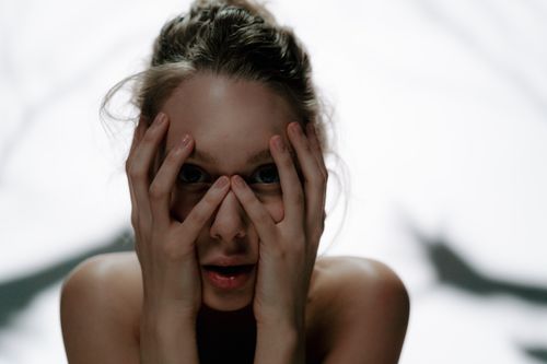 Free Close-up of a woman with hands covering face, expressing intense emotion with shadows in the background. Stock Photo