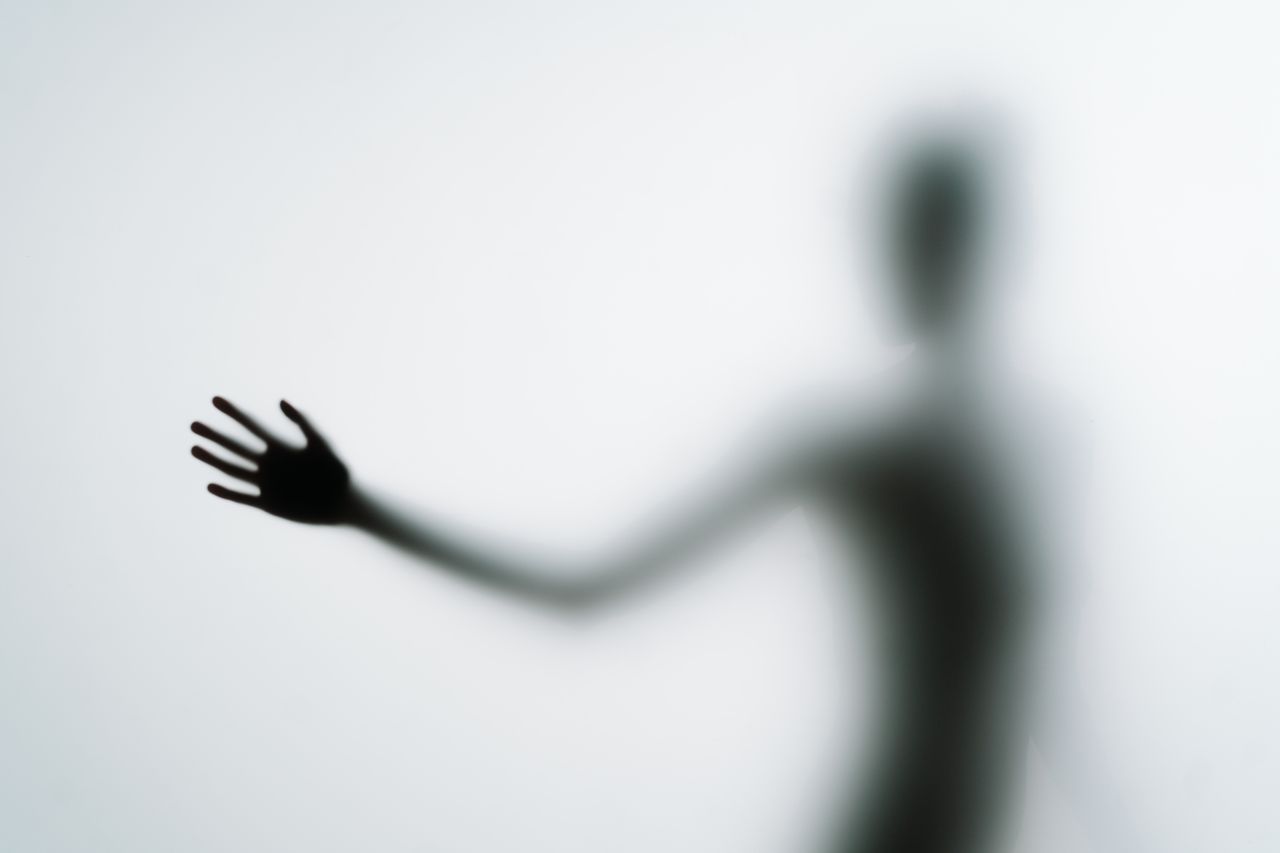 blurred silhouette of a hand reaching out against a light background i