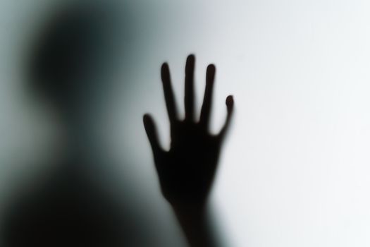 Silhouette of a hand pressed against frosted glass, creating a mysterious atmosphere.