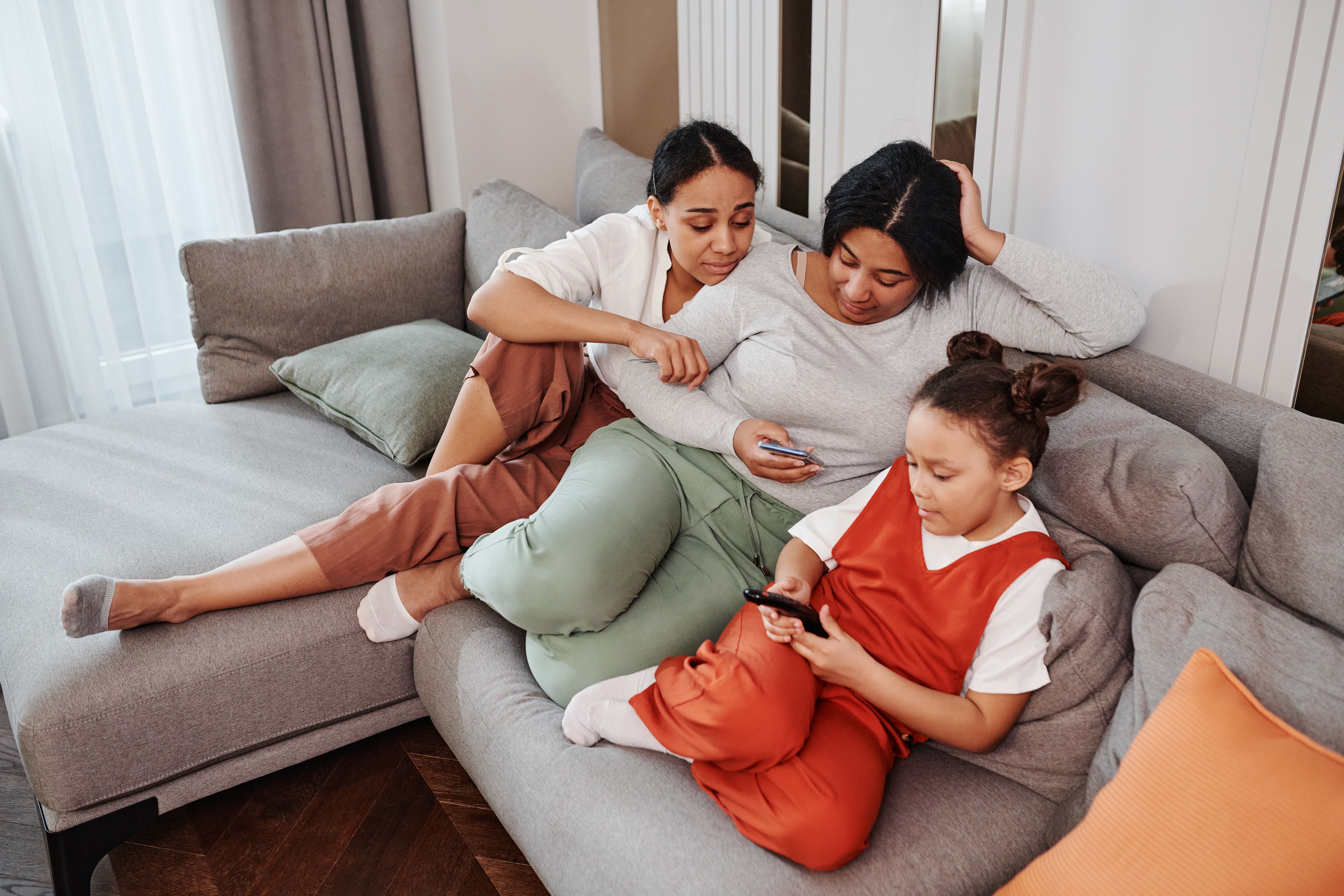 A mother, daughter, and family friend enjoy quality time together on a living room sofa.