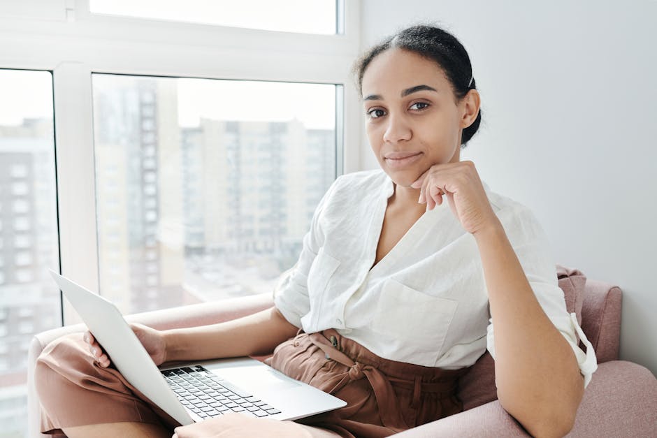 Woman sitting on an armchair using a laptop indoors by a window.