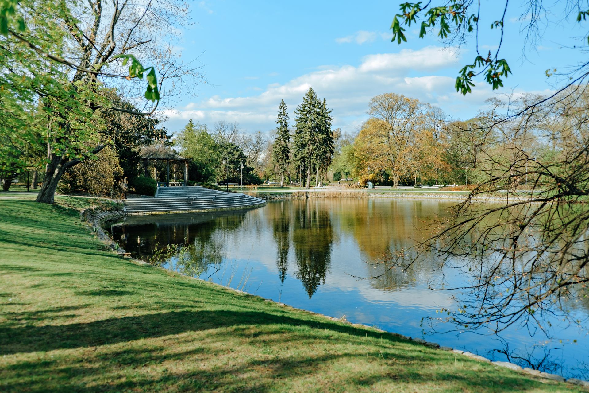 Peaceful park scenery with a gazebo and reflective pond surrounded by lush trees.