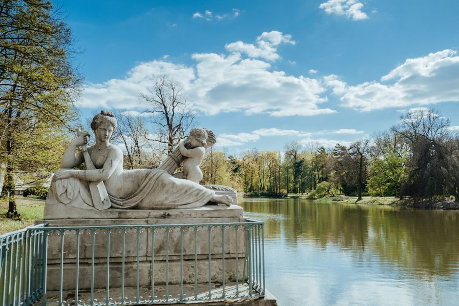 A serene statue by the lake in Wilanów Park, Warsaw under a bright spring sky.