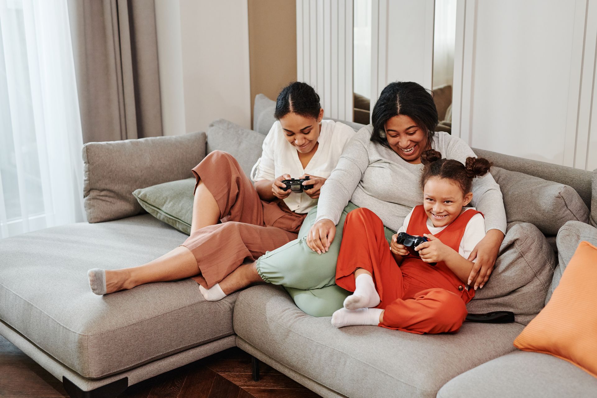 A joyful family moment as mother and daughters play video games together on the couch.