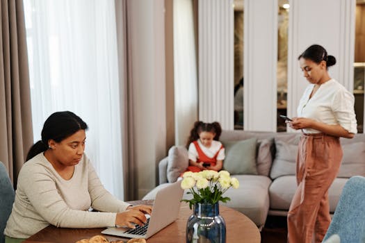 A woman works on a laptop while others use devices in a cozy living room setting.