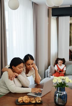 A couple enjoys their time working on a laptop at home while a child plays in the background.