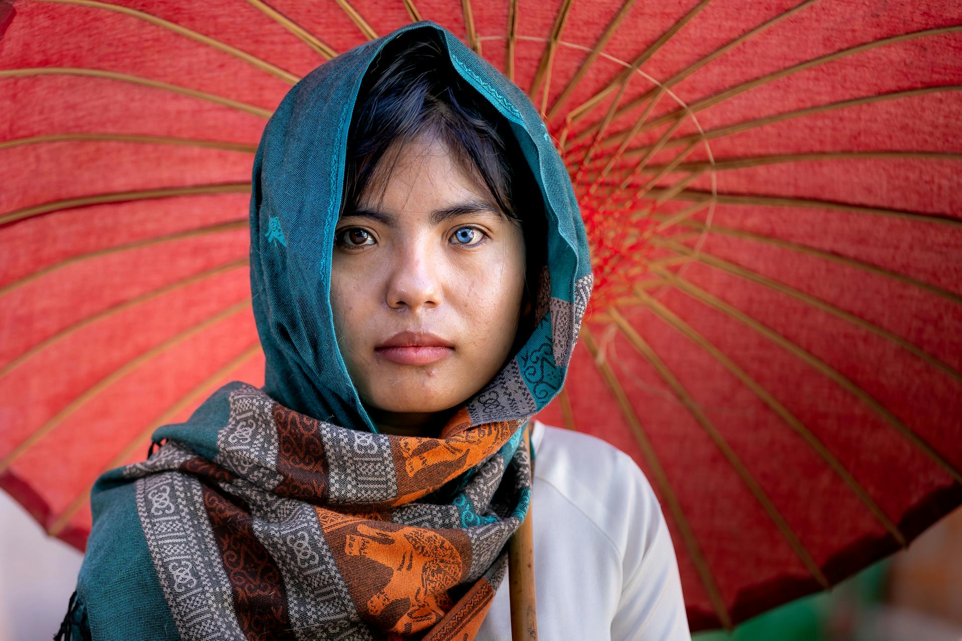 Close-up of a woman wearing a hijab with heterochromia under a vibrant umbrella.