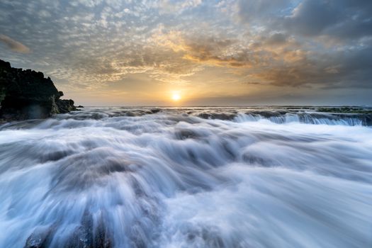Stunning ocean waves cascade as the sun sets, creating a dramatic natural scene.