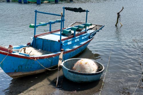Free Vibrant blue fishing boat moored with nearby coracle and fishing net on a calm water body. Stock Photo