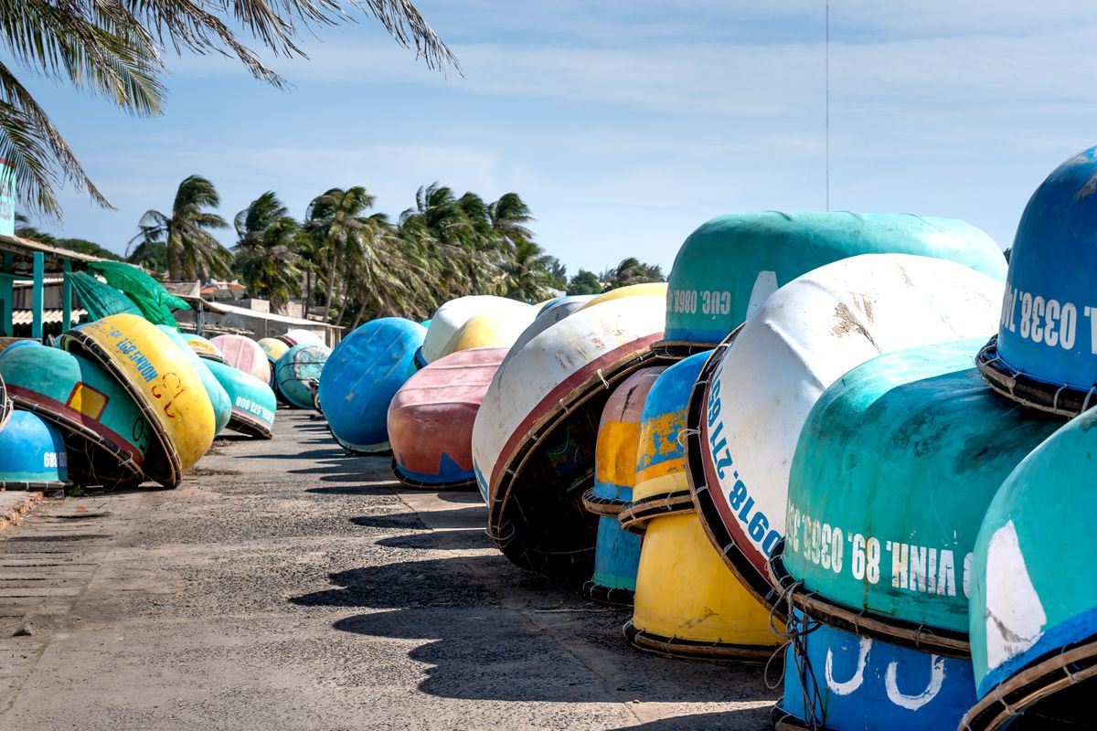 Colourful round fishing boats stacked beside palm trees in Mui Ne