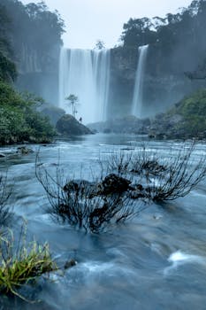 A stunning waterfall cascading down cliffs surrounded by a misty forest in a tranquil setting.