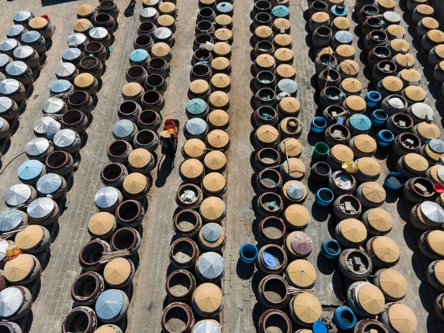 Aerial view of numerous industrial barrels organized in neat rows outside under sunlight.