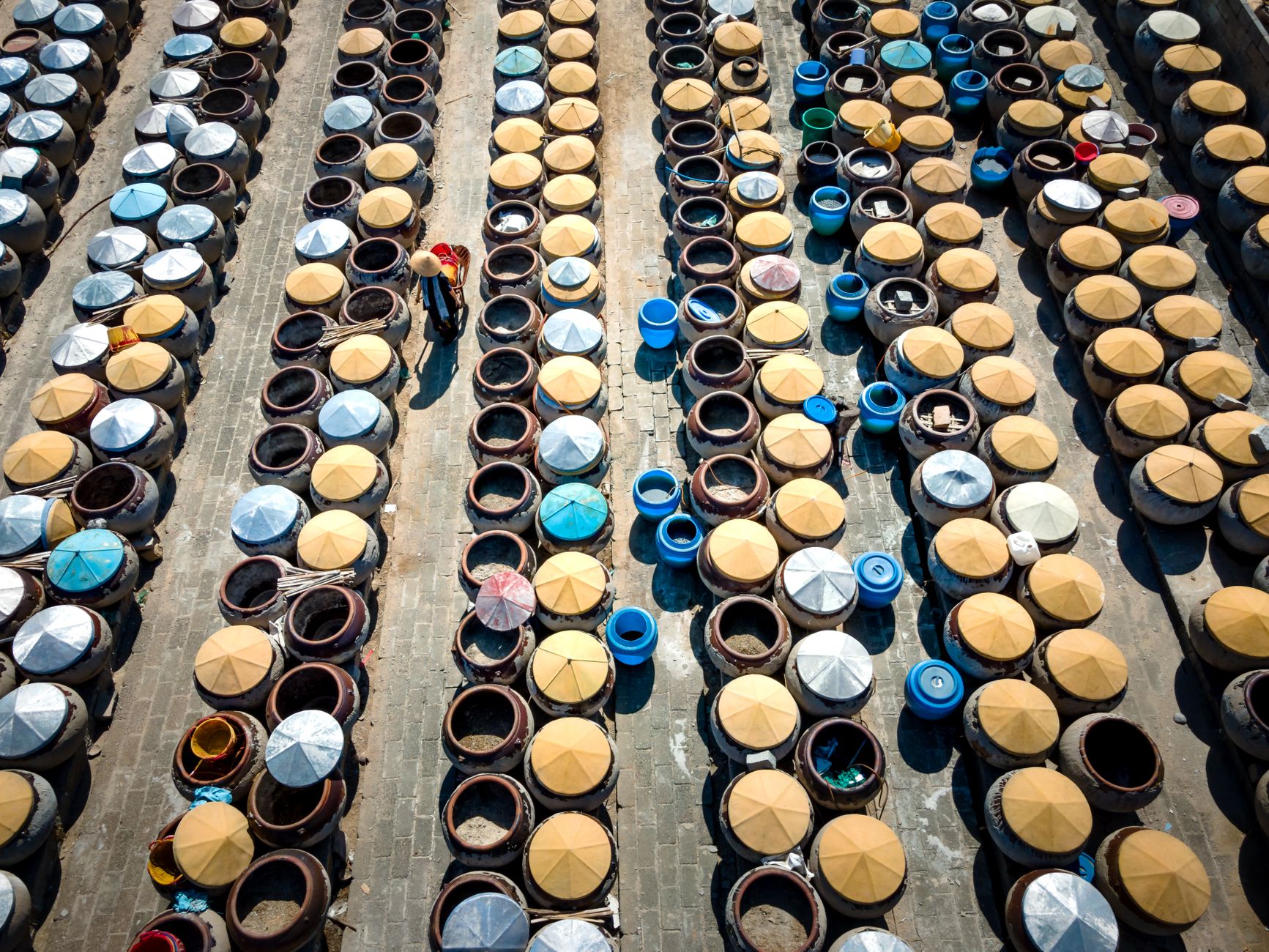Drone shot of traditional fish sauce factory with large fermentation barrels outdoors.
